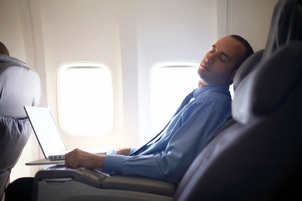 Business man sleeping on airplane with laptop on lap