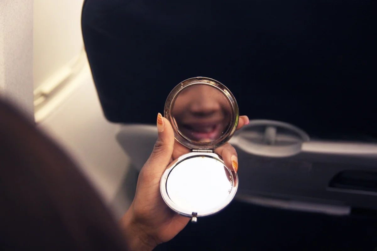 Young woman looking at the pocket mirror inside the airplane