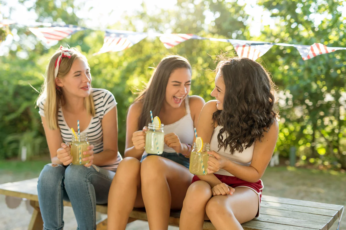 Three friends drink iced lemonade together from mason jars