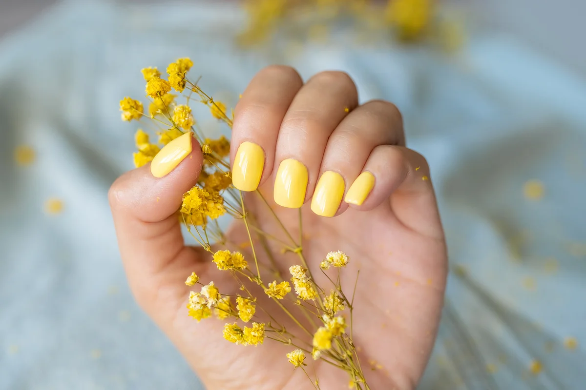 Yellow manicure with a nail polish bottle in hand