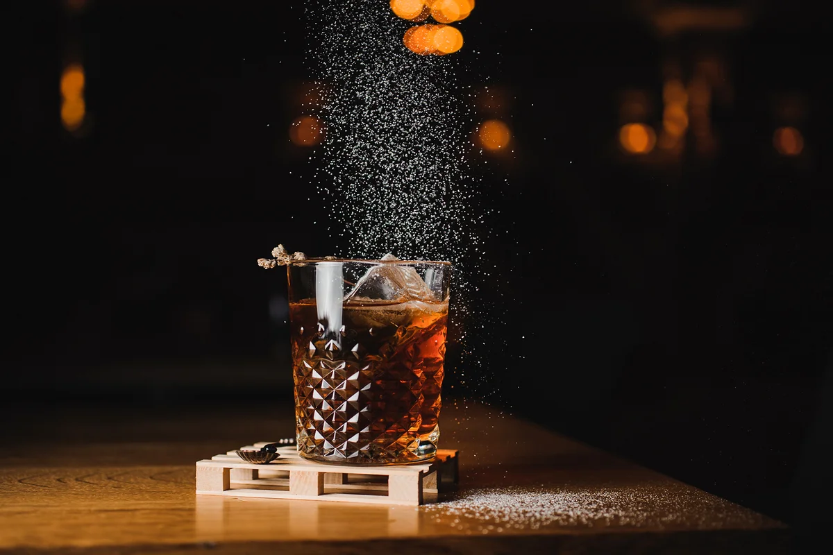 Dusting whiskey drink with ice on wood in bar
