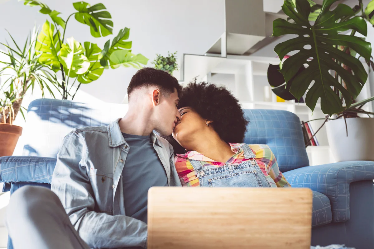 Young couple kissing on mouth with laptop in living room