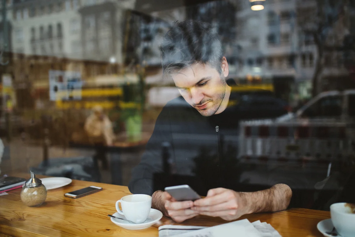 Young man relaxing in a cafe in Berlin, texting on the cellphone