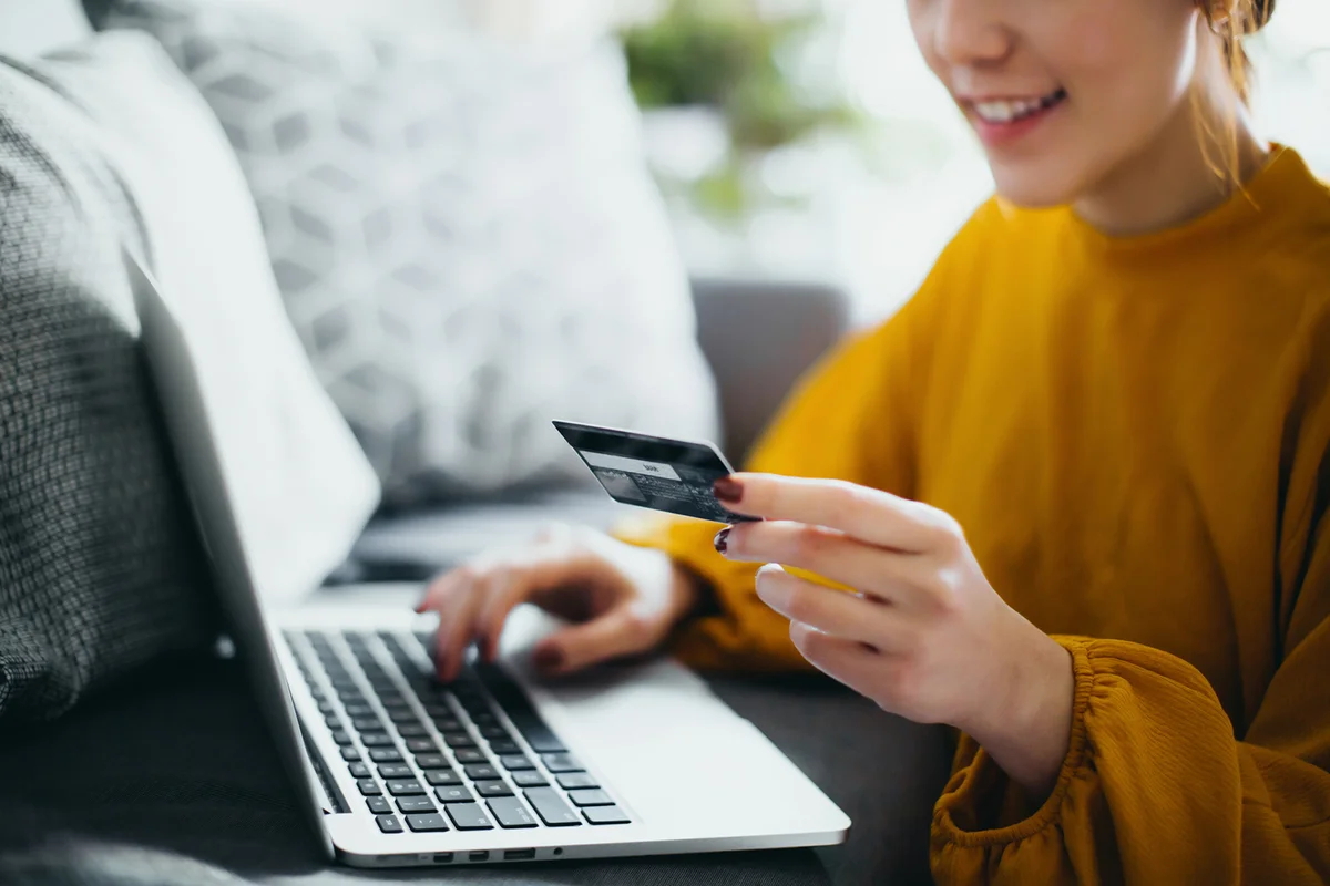 woman sitting on the floor by the sofa, managing financial bill payment with laptop and credit card on hand