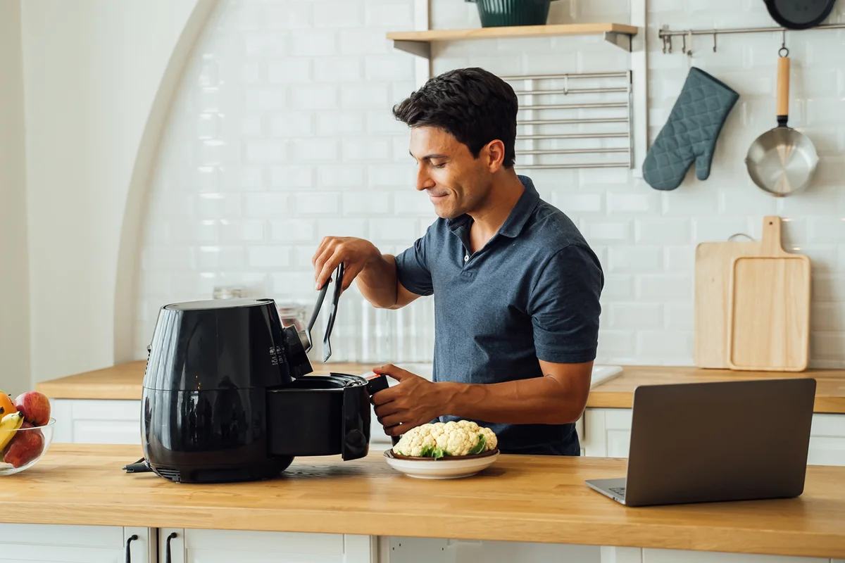 Man using air fryer and laptop in kitchen