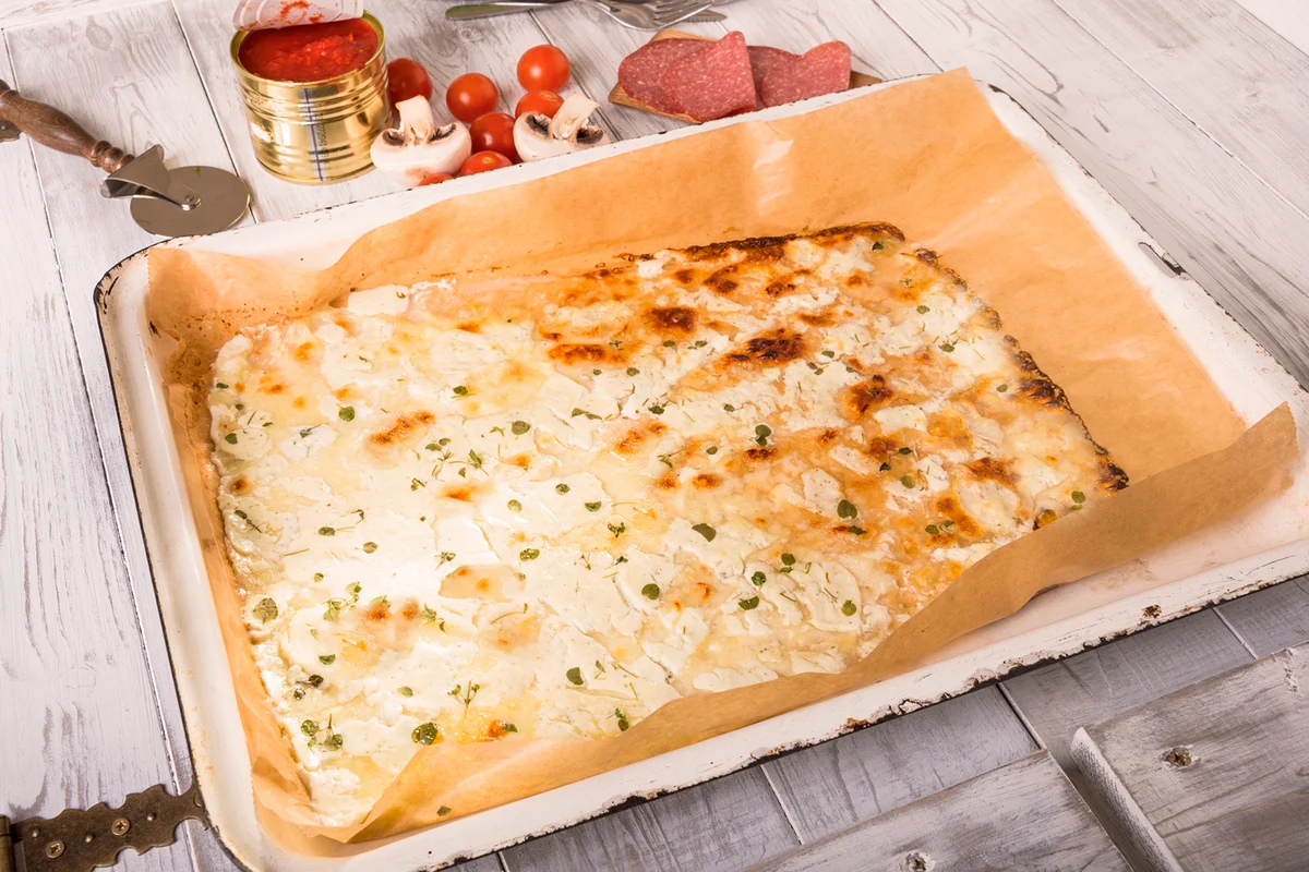 Baking tray of low carb pizza base on wooden table with mozzarella