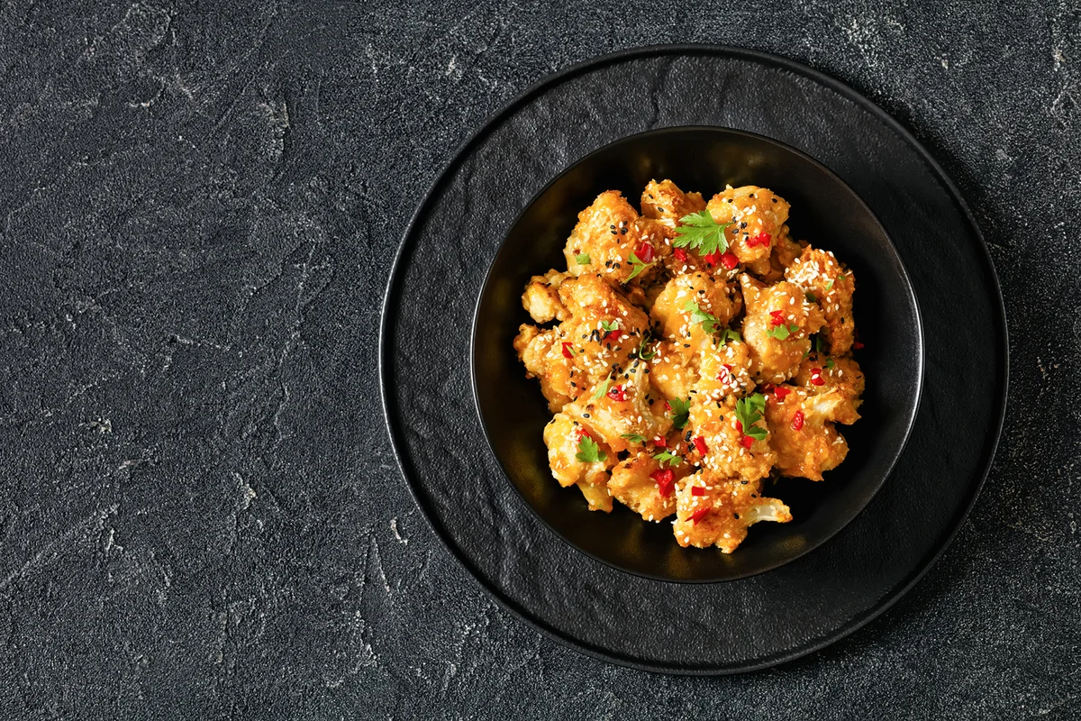 Crispy orange cauliflower florets in black bowl