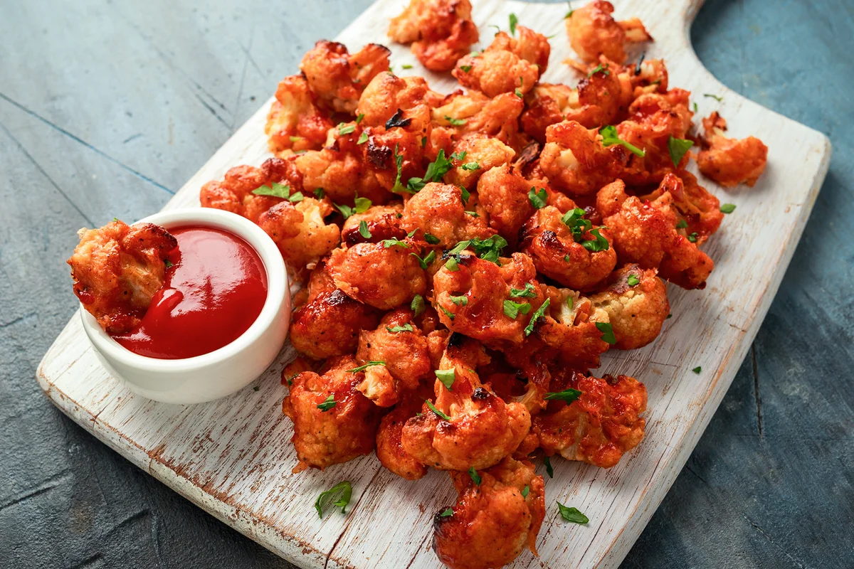 Vegan cauliflower buffalo wings on white wooden board