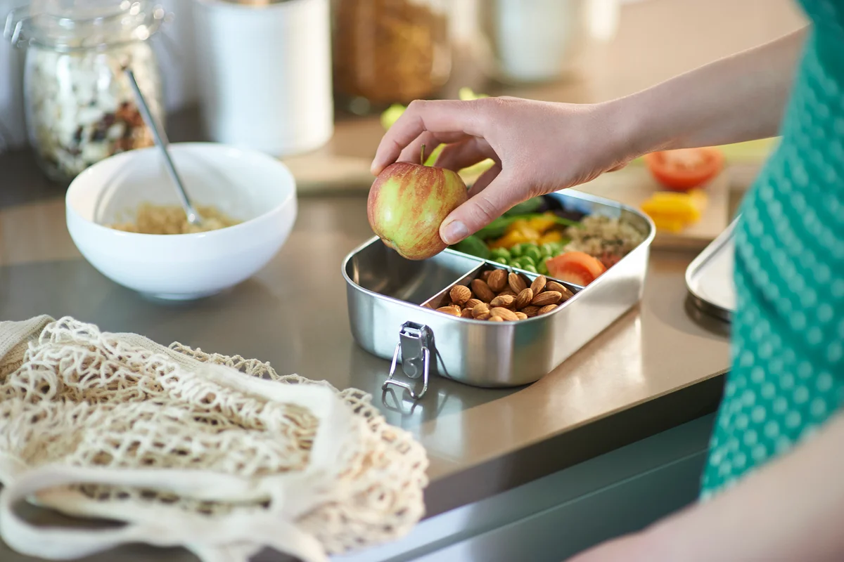 Woman packing vegan food into plastic free lunchbox at home
