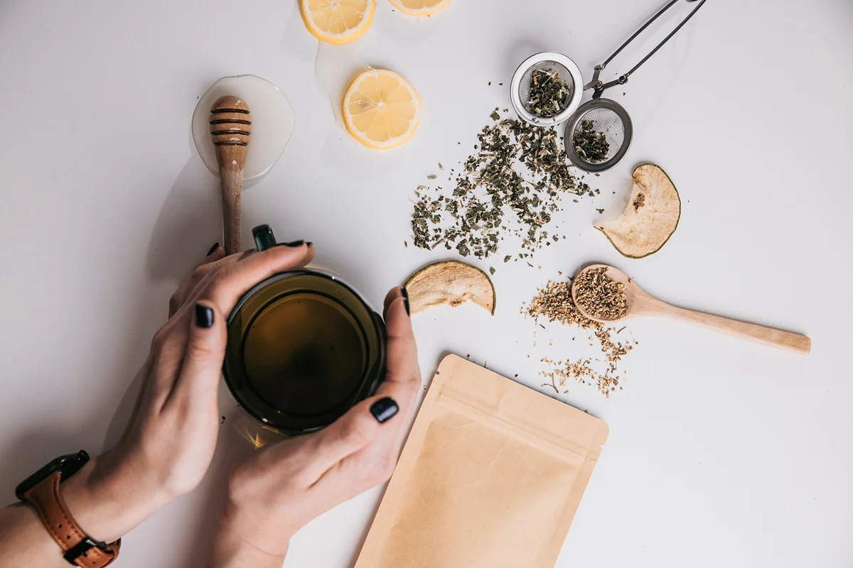 Woman hands hold glass cup of tea on table with other tea props