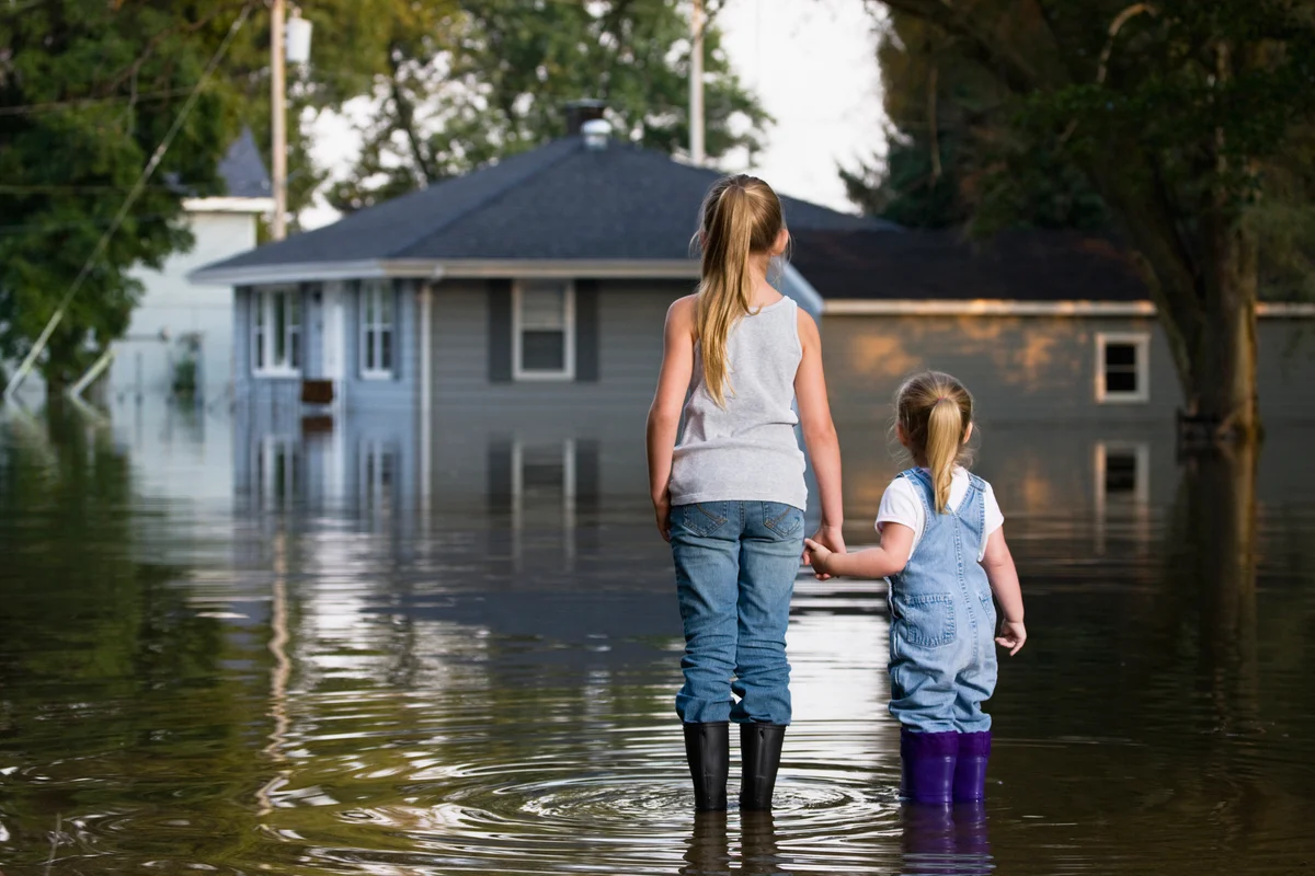Two little girls standing outside looking at flooded house