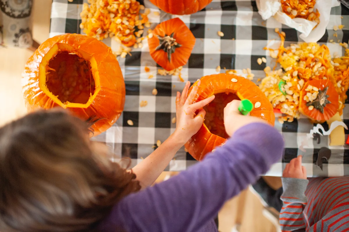 Woman carving pumpkins with guts and seeds all over table