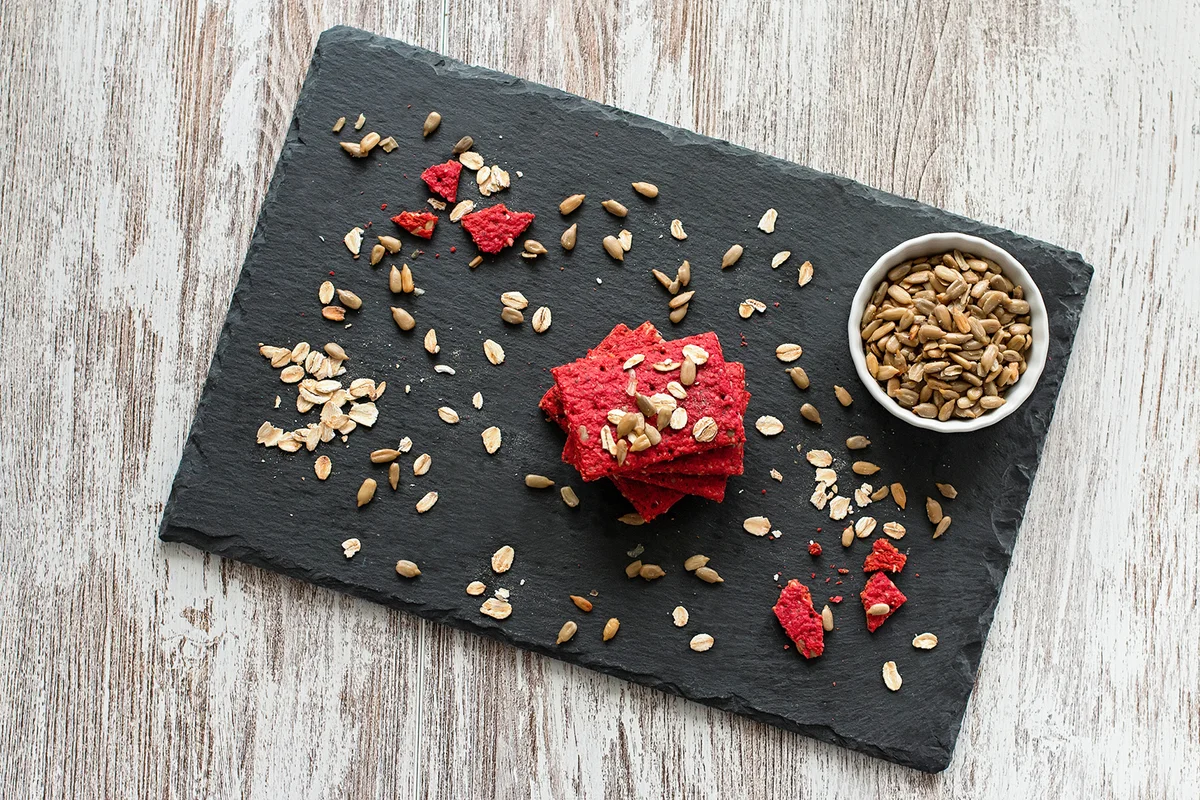 Healthy snack cracker or biscuit with seeds and beetroot top view on a stone plate with oat flakes