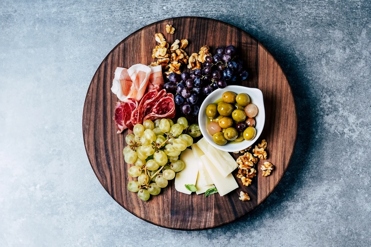 Antipasto (cheese, olives, salami, prosciutto, walnuts, and grapes) on wooden cutting board