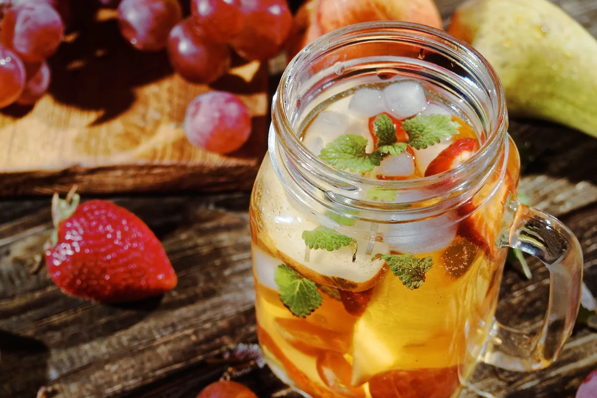 Cold fruit drink in mason jar surrounded with various fruits