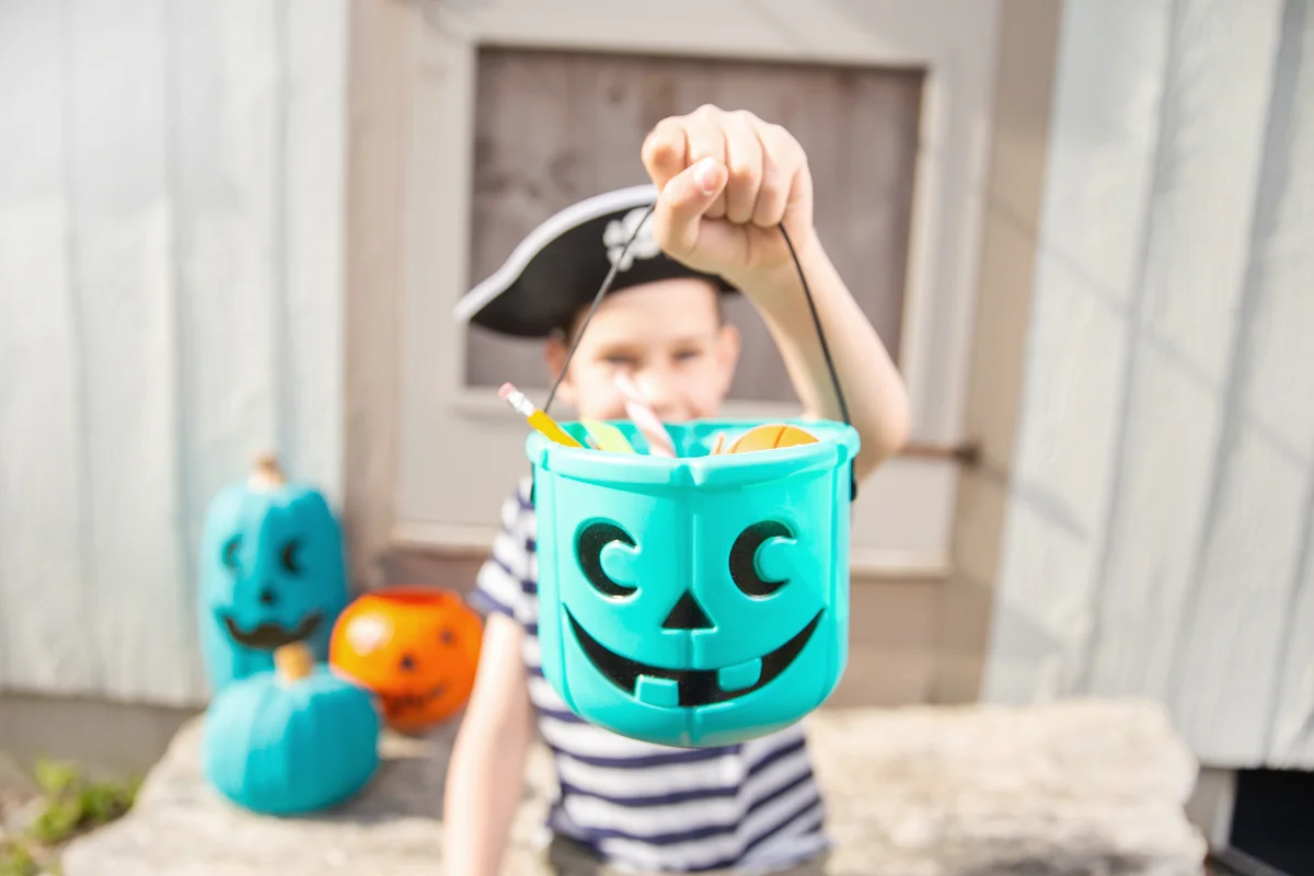 Boy in a pirate costume holds a teal bucket