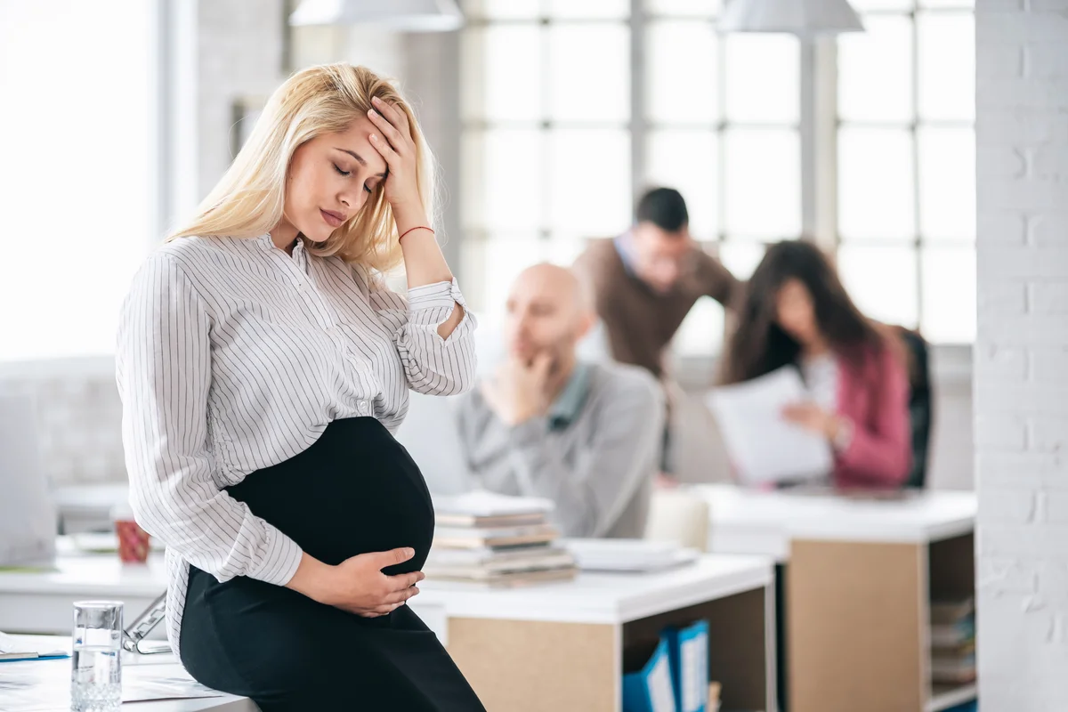 Pregnant woman looking dizzy at work, holding her head