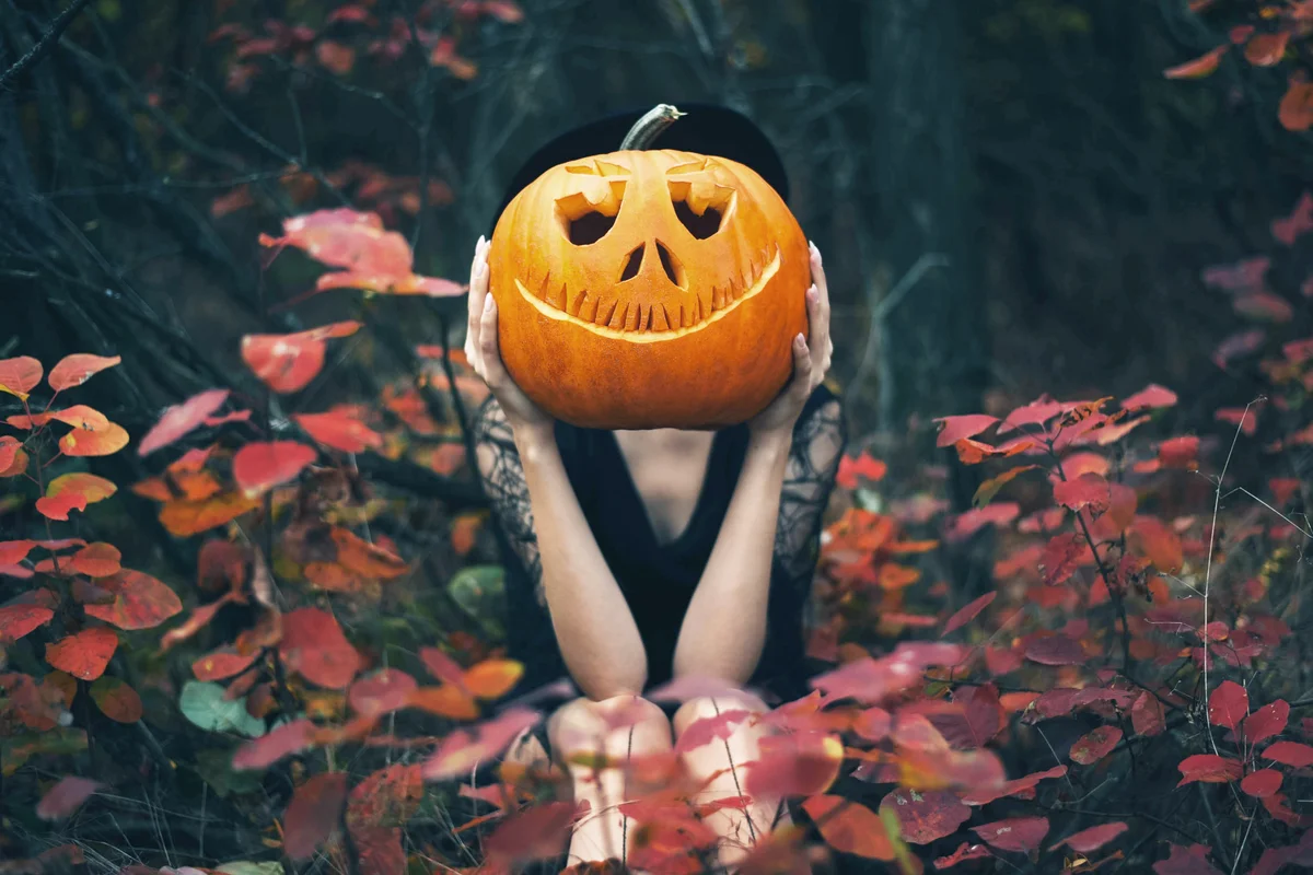Woman sits in the forest and holds a pumpkin in her hands