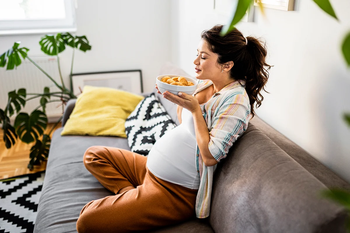 Young pregnant woman siting on sofa craving for food at home