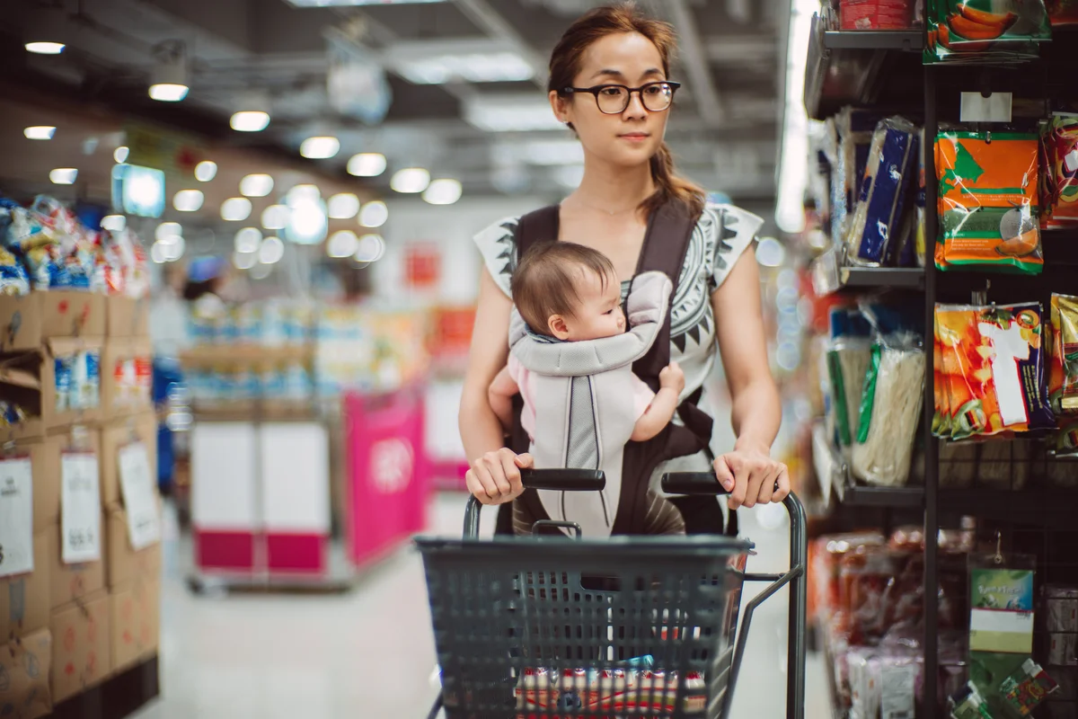 woman grocery shopping with baby strapped to chest