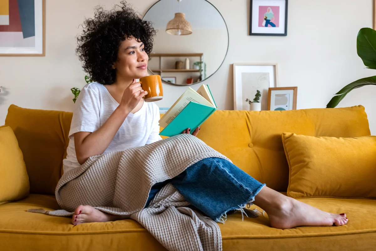 Woman on couch drinking coffee and reading book