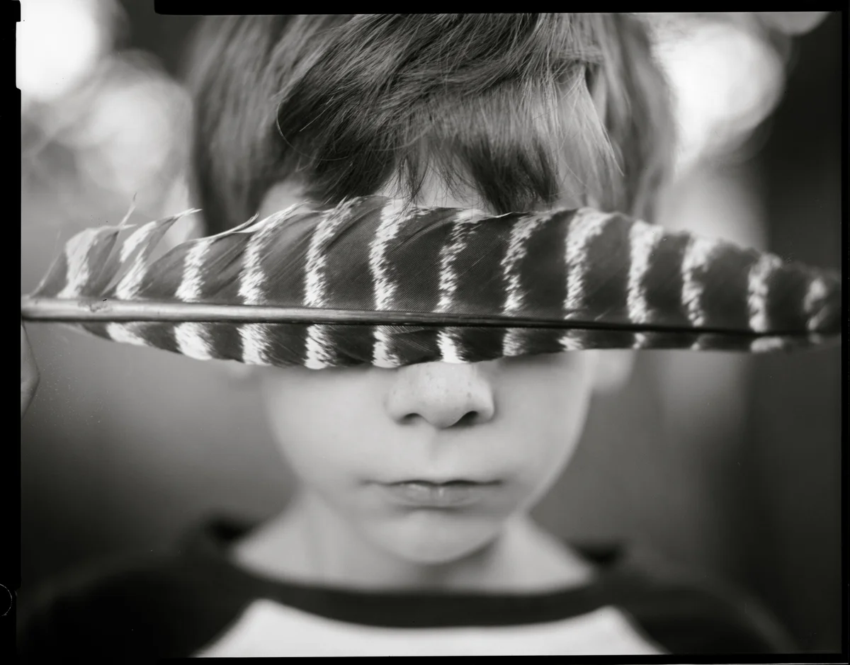 black and white film photograph of boy with feather covering eyes