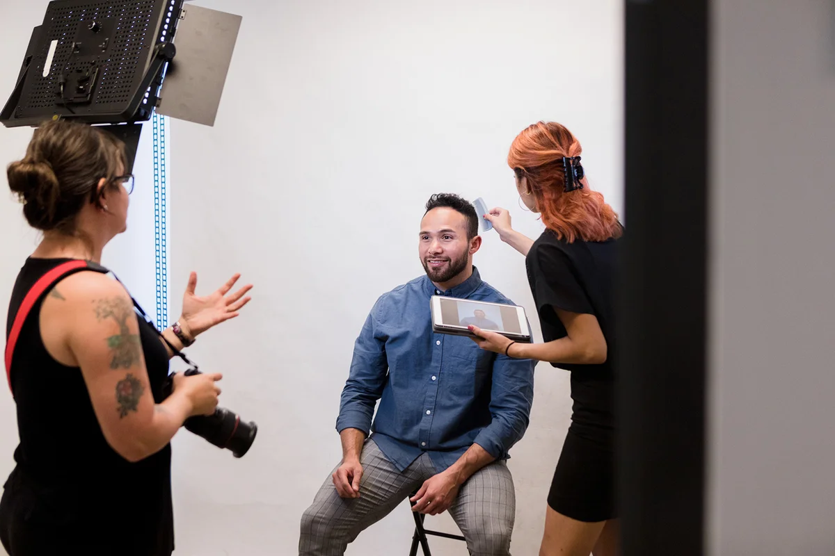 Female assistant helps female photographer prepare businessman for photoshoot