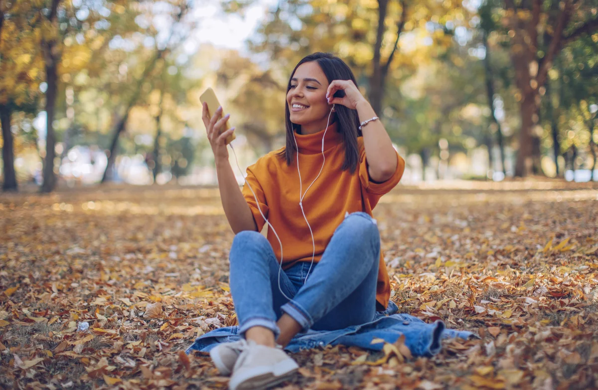 Woman sitting in autumn leaves while she listens to music