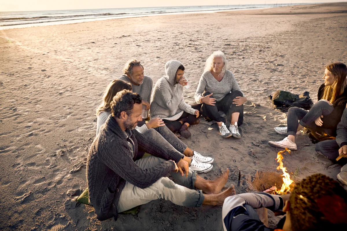 Group of friends sitting around campfire on the beach at sunset