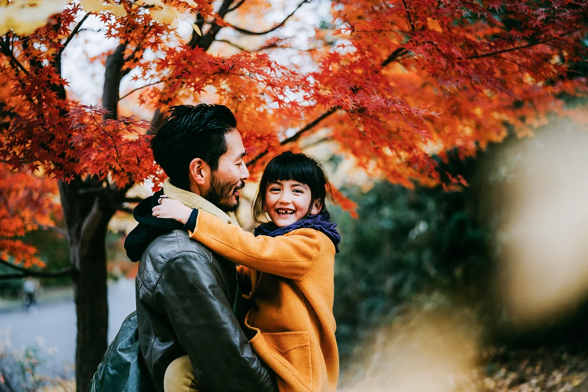 Father holding cute little girl under autumn leaves