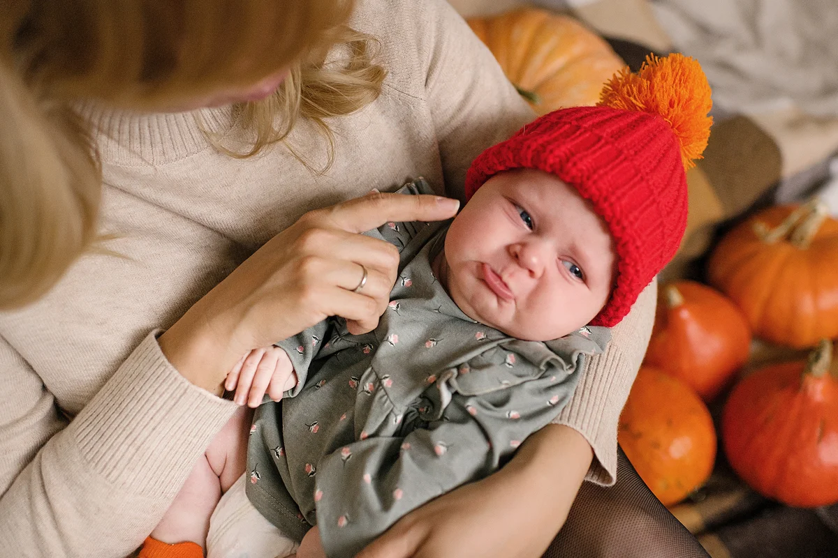 Upset baby girl in mothers hands with pumpkins in seasonal autumn