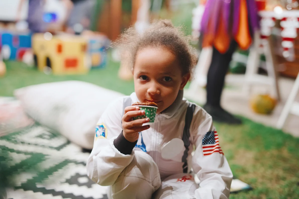 Cute little astronaut girl eating cupcake during Halloween