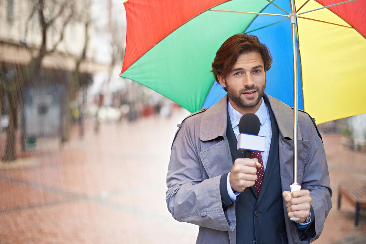 A smiling weatherman reporting from an urban area