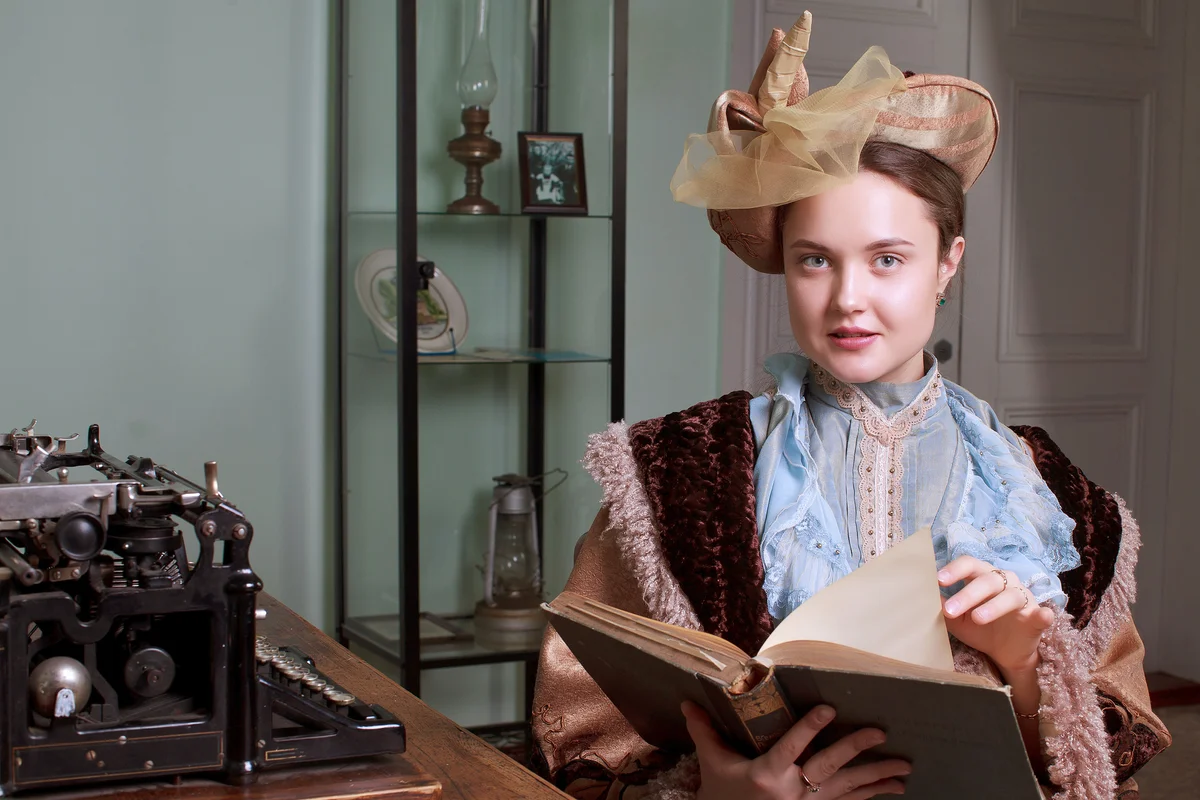 Young woman in blue vintage dress late 19th century reading a book