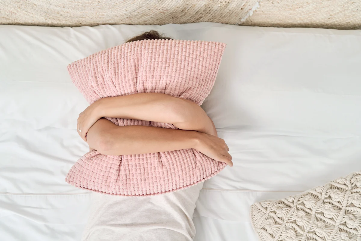 Young woman lying in bed covering her face with a pillow