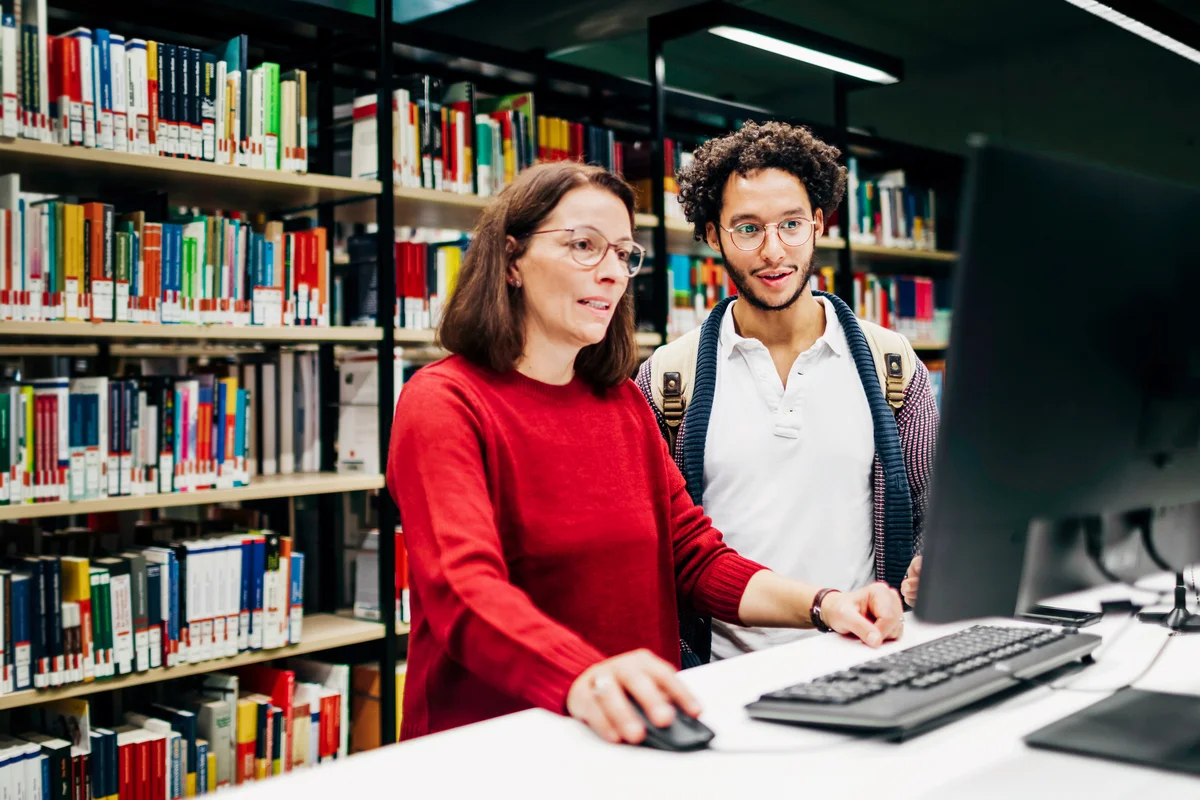 Librarian Looking Up Books On Computer For Student