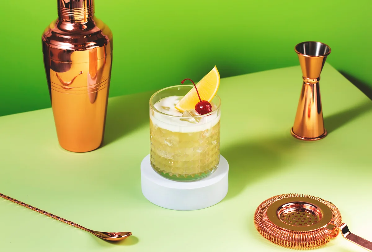 Whiskey sour cocktail with bourbon, lemon juice, egg white and ice, rocks glass on bright green background