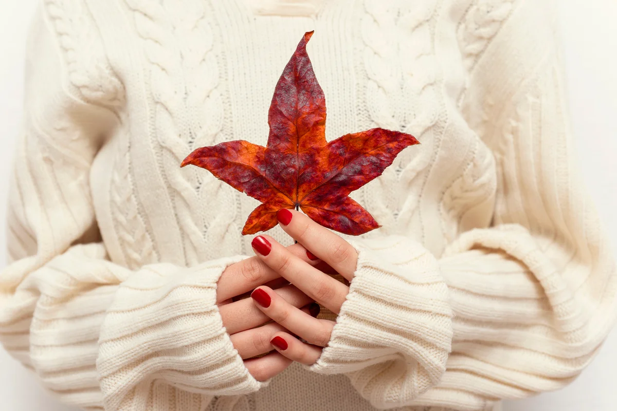 Woman's hands with autumn red leaf and red nails