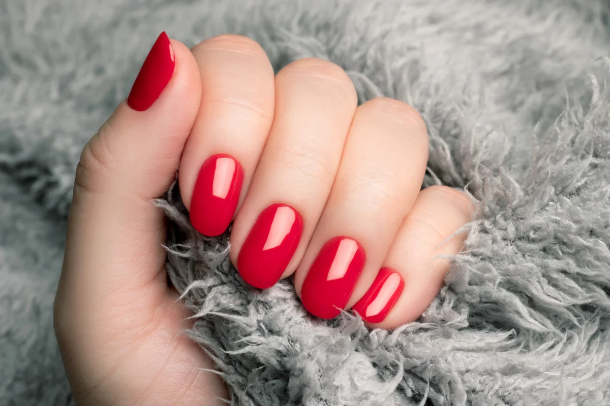 Hand with poppy red nails on gray fluffy fabric