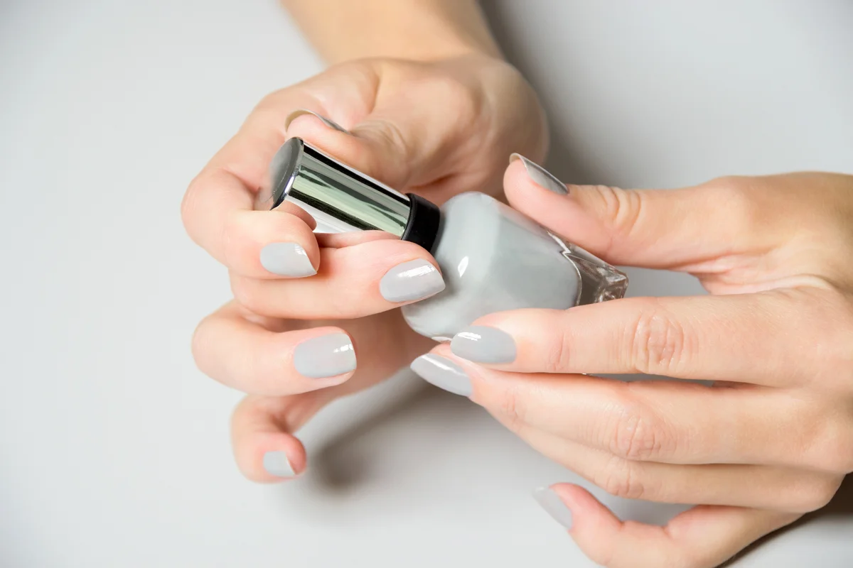 Hands with powder gray nails opening nail polish bottle