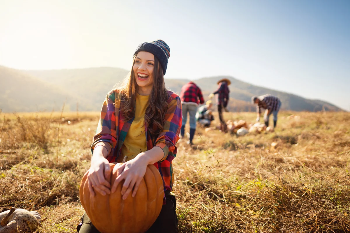 One happy young female farmer harvesting pumpkins on the field
