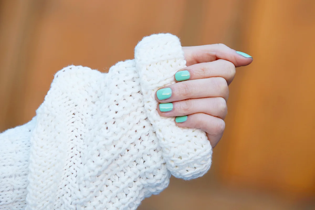 Woman's hands in winter gripping knitted sweater with mint green nail polish