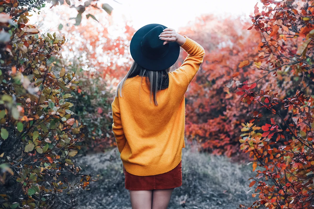 A girl stands with her back in a hat on nature in autumn