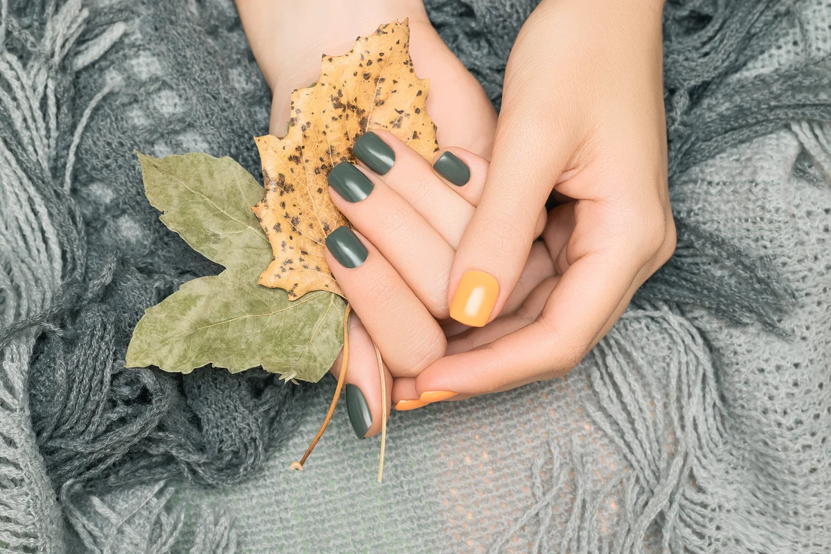 Female hands with sage green and yellow autumn nail design