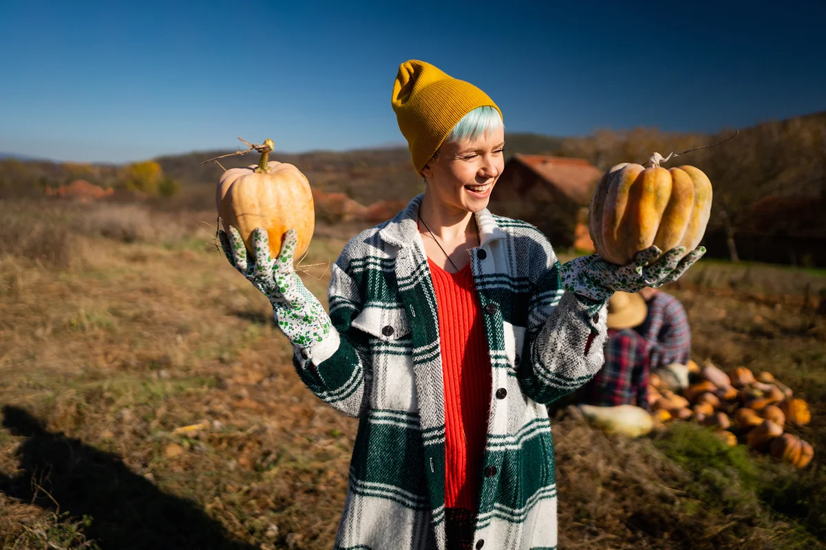 Portrait of happy female farmer with pumpkins on the field