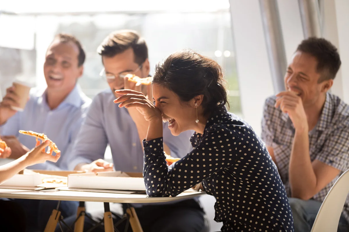 Woman laughing eating pizza with coworkers in office