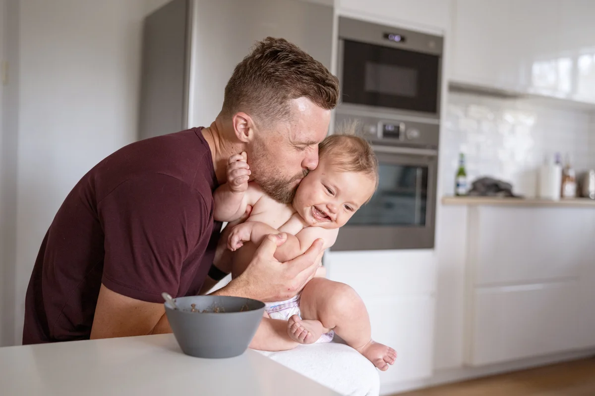 Father kisses son on the cheek while feeding him lunch