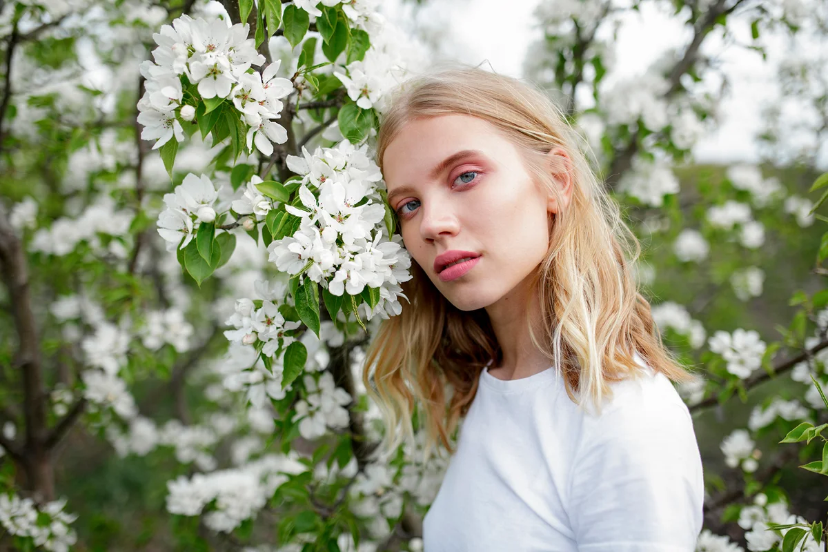 Blond haired young woman among white blossoms
