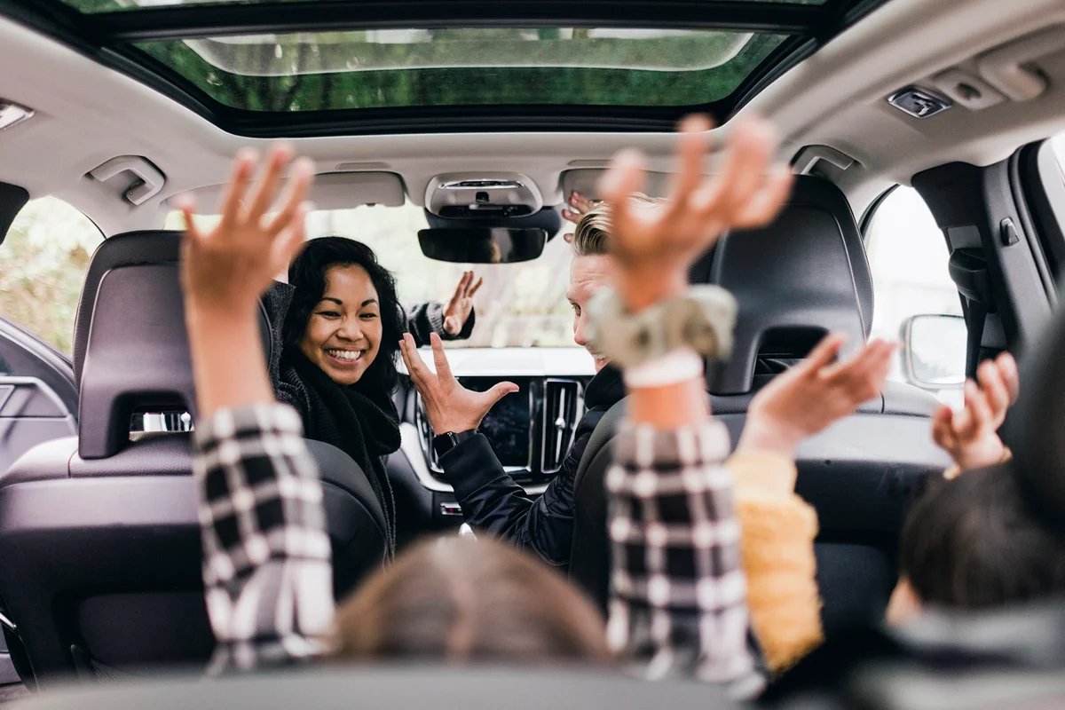 Cheerful family raising hands while enjoying road trip in electric car