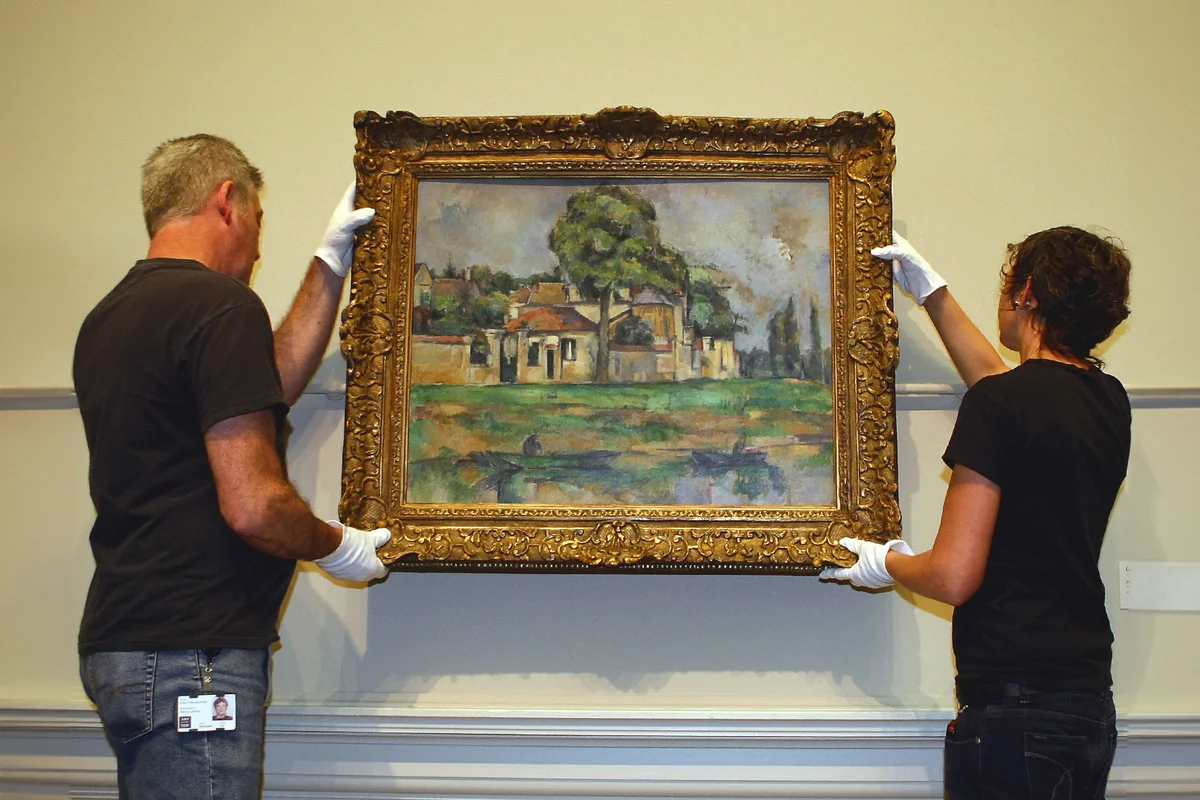 Attendants hang 'Bords de la Marne c1888' by French Impressionist, Paul Cezanne, on the walls of the Art Gallery of New South Wales in Sydney
